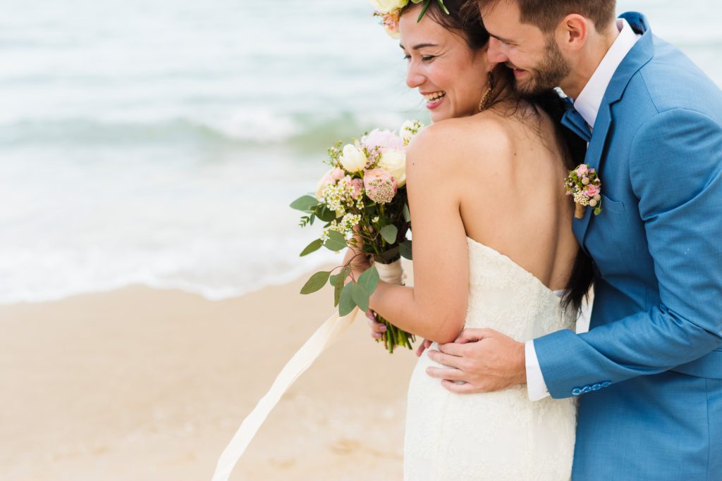 Smiling bride and groom embracing on the beach at their destination wedding